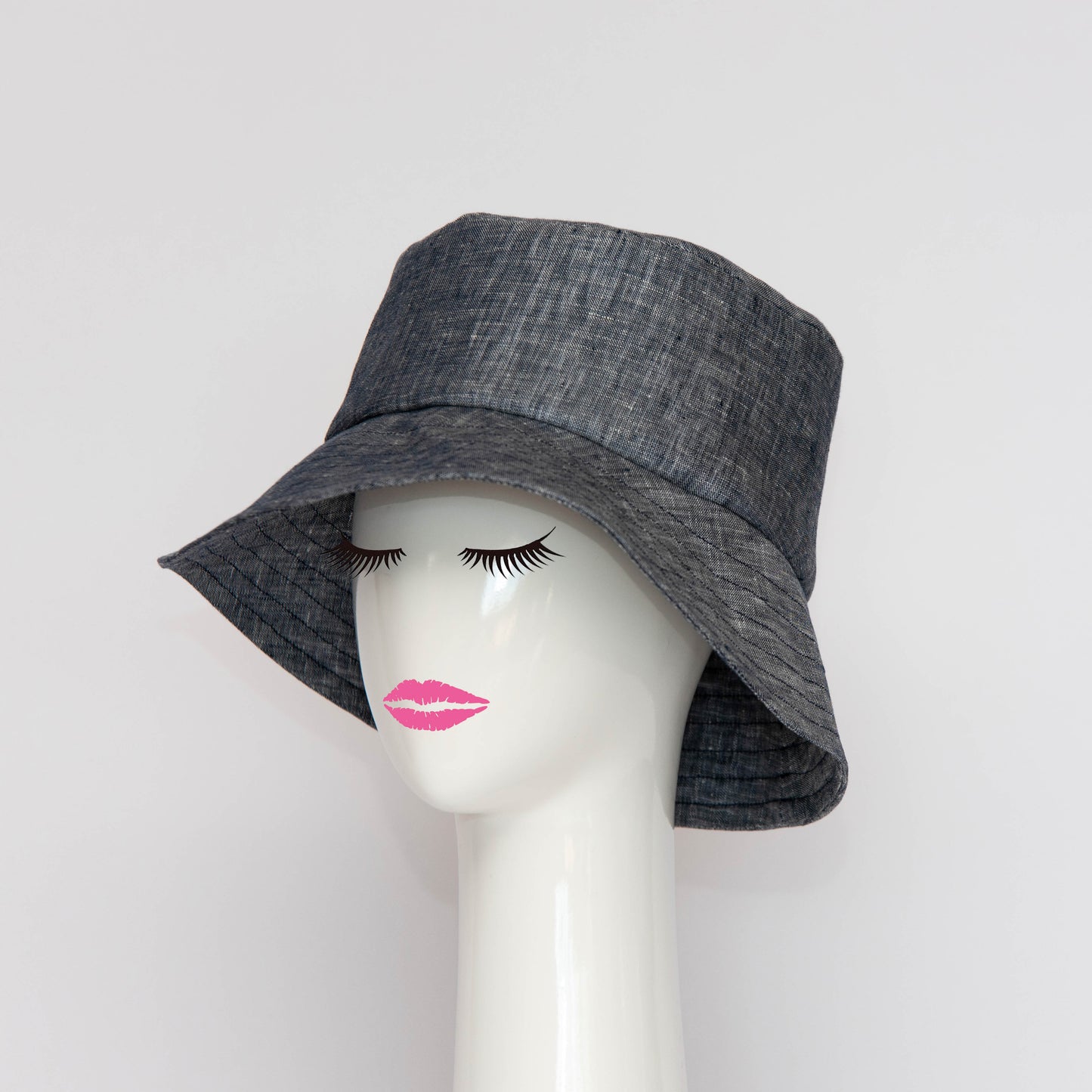 The Appin Bucket Hat in denim has a square shape crown with tip and side band. The picture shows the hat on an angle, showcasing the flared brim which protects you from the sun. Created by Melbourne based Lauren J Ritchie Millinery.