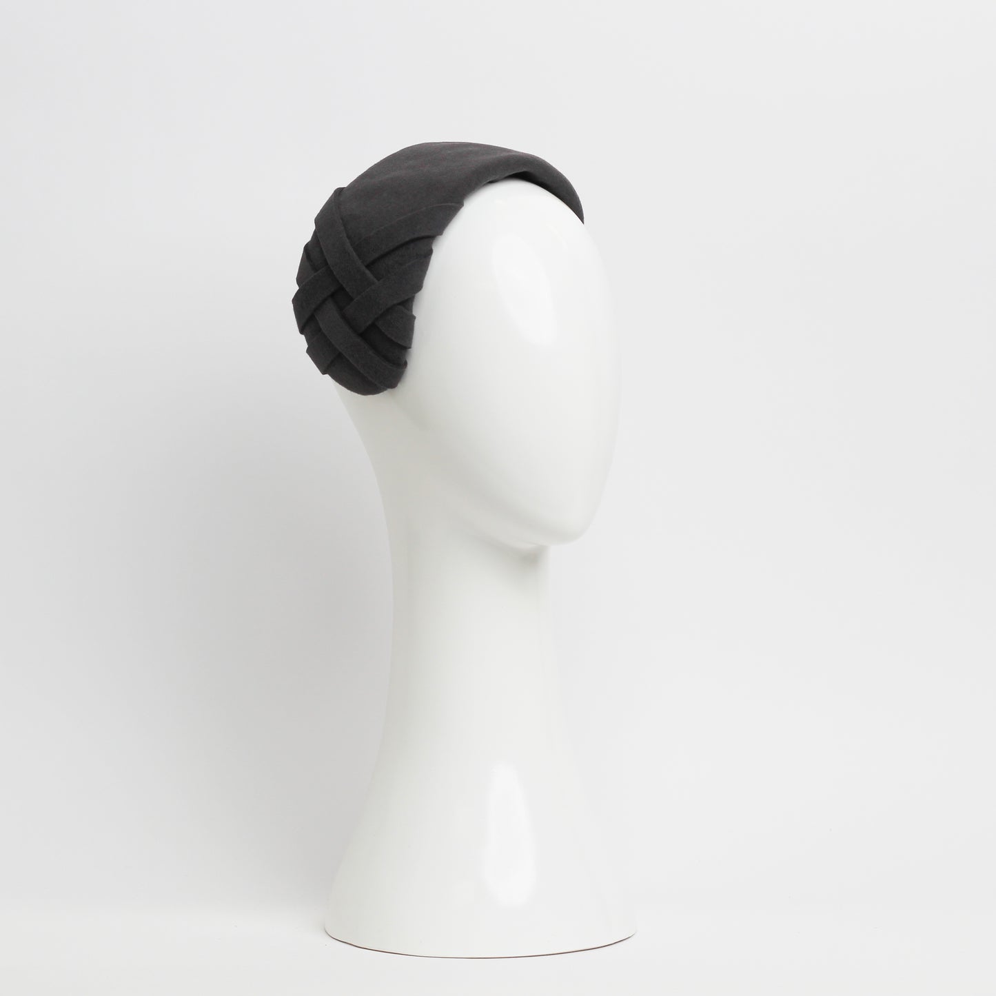 The front view of a grey felt headpiece that sits flush to the head with a small weave trim on the right hand side 