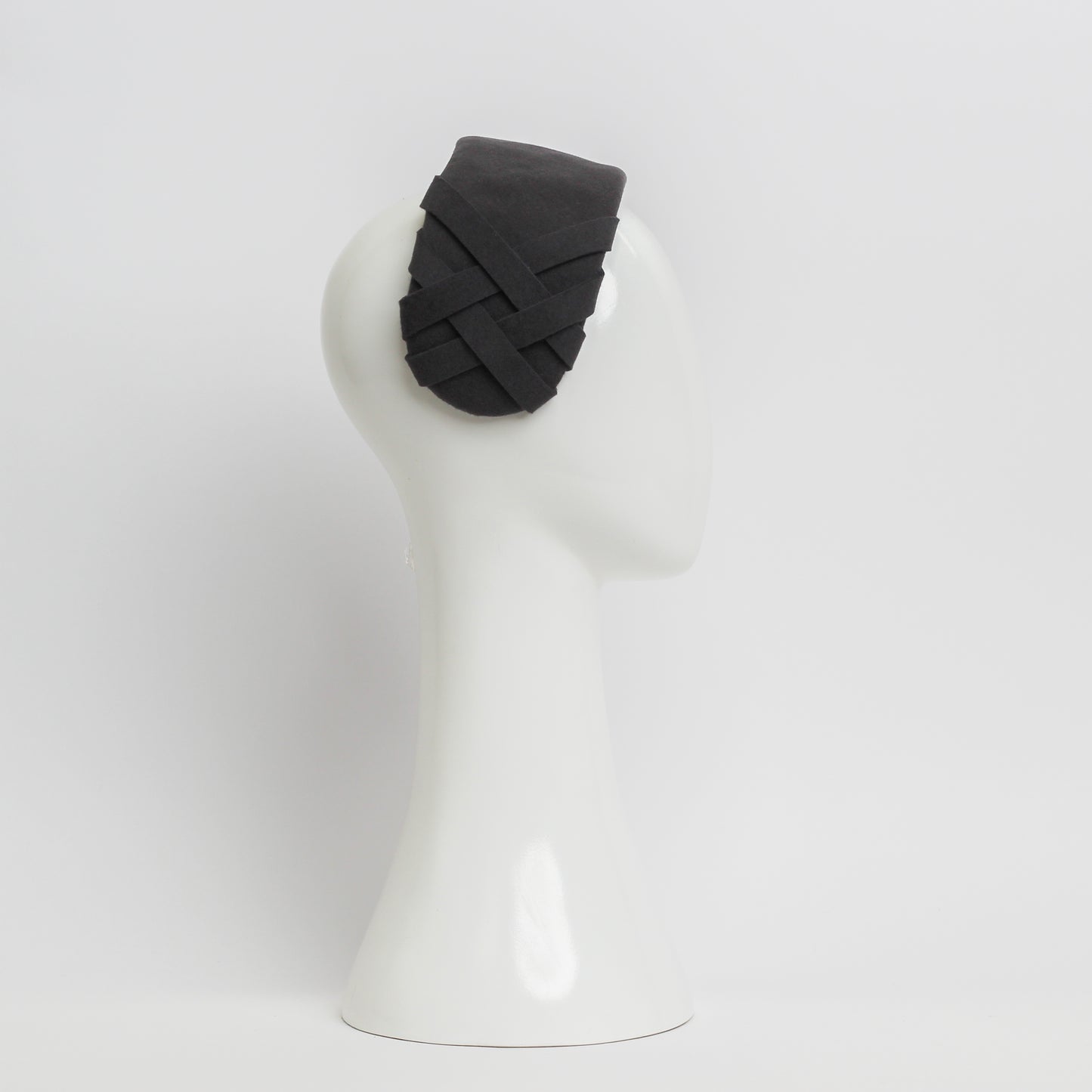 The side view of a grey felt headpiece that sits flush to the head with a small weave trim on the right hand side 