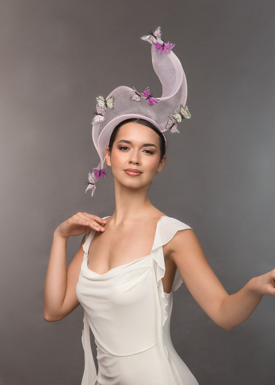 A model wearing a decorative pale pink crinoline headpiece with butterflies against a gray background