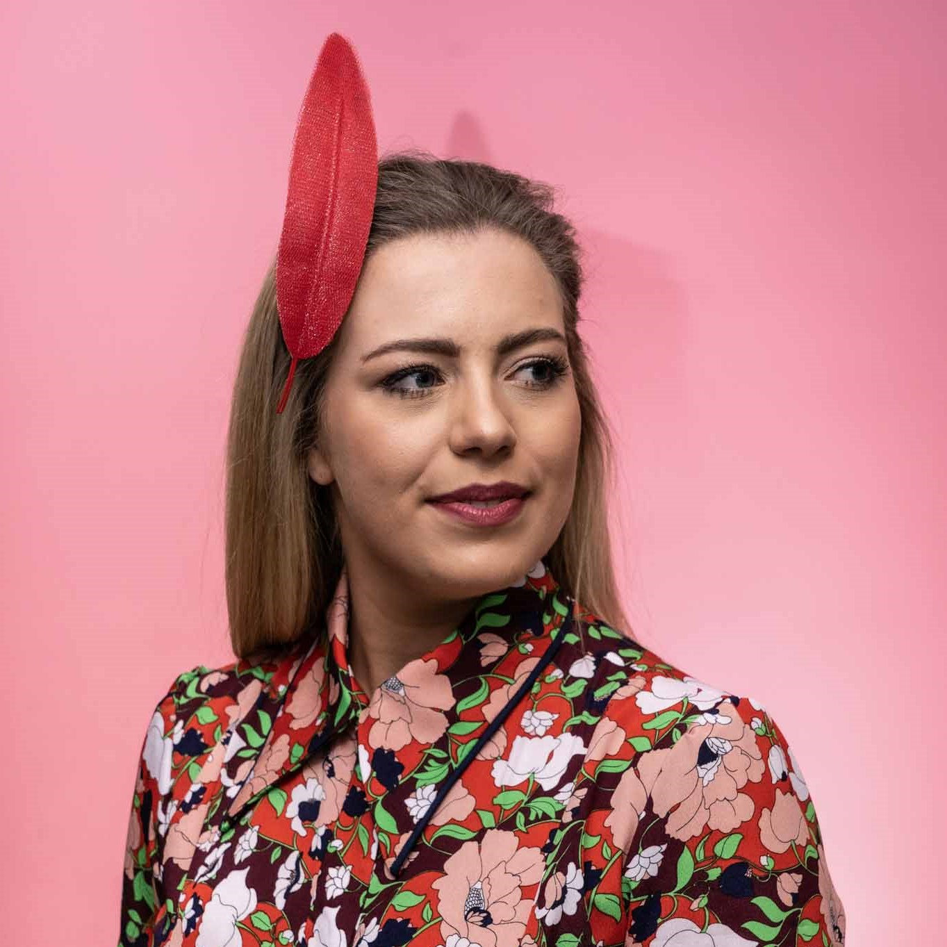 A photo of a model wearing the Alba Headband in red. This headpiece features a floating tulle feather secured to the head by a headband. Created by Melbourne based Lauren J Ritchie Millinery.