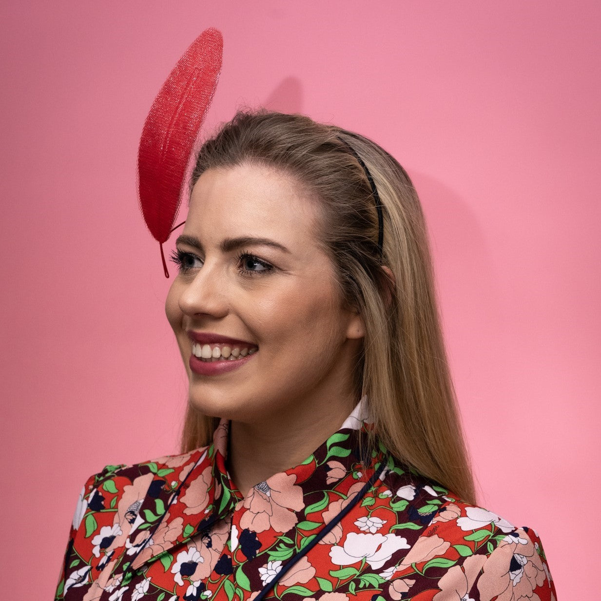 A side view of a model wearing the Alba Headband in red. This headpiece features a floating tulle feather secured to the head by a headband. Created by Melbourne based Lauren J Ritchie Millinery.